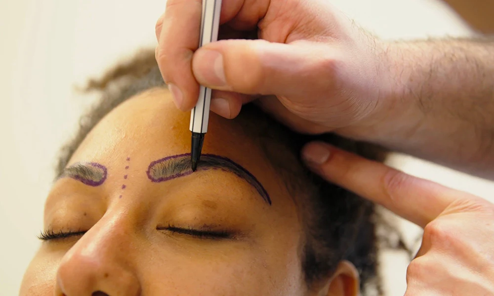 پزشکی که روی ابروی زن مراجعه کننده خط می کشد - کاشت ابرو پهن